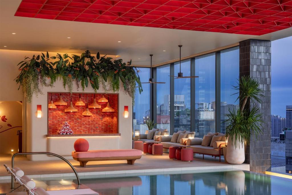 A rooftop pool lounge combining skyline windows, a red ceiling, and relaxed seating.
