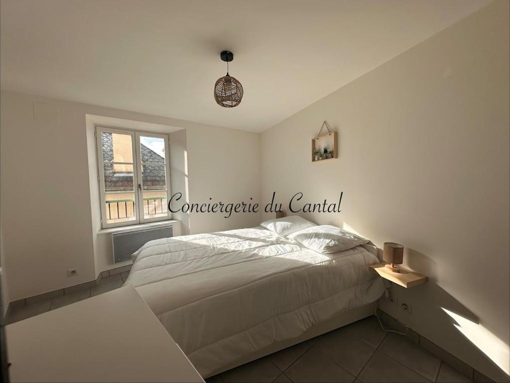 a white bedroom with a bed and a window at Murat - La petite maison Murataise in Murat