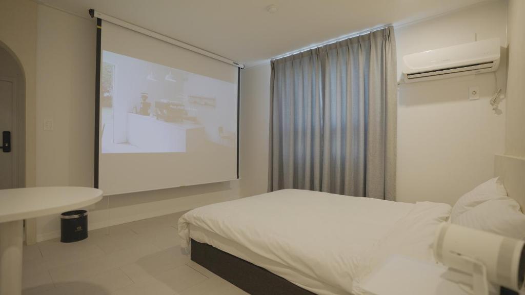 a bedroom with a white bed and a projection screen at Jeju Stay Hotel in Jeju
