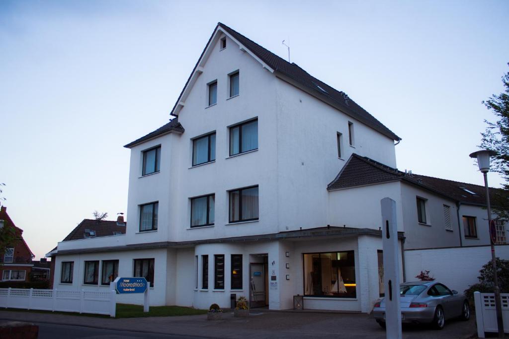 Hotel Meeresfriede في كوكسهافن: مبنى أبيض فيه سيارة متوقفة أمامه