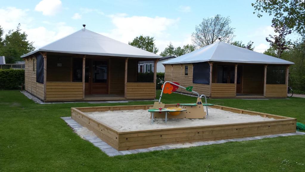 a small house with a sandbox in the yard at Lodge 6 personen op Camping Mounewetter in Witmarsum