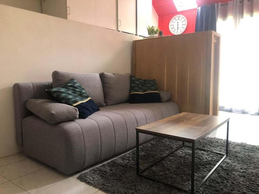 a living room with a couch with a table and a clock at Studio gare et commerces sur place in Nogent-lʼArtaud