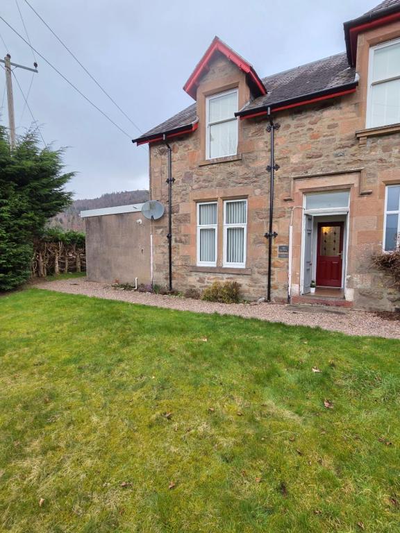 a brick house with a red door and a yard at Ardgay in Fort Augustus