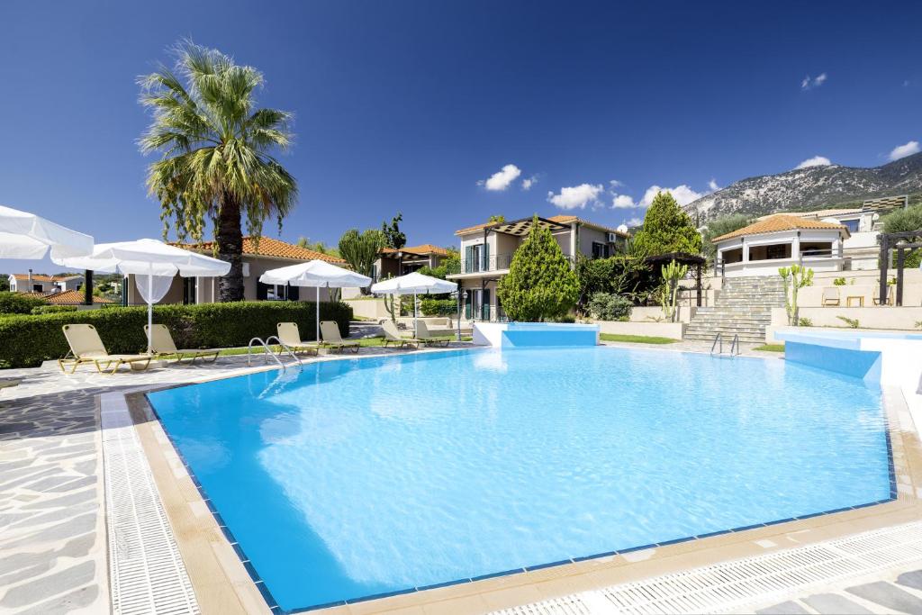 a large swimming pool with a palm tree and houses at Kefalonian Oneira Villas in Mousata