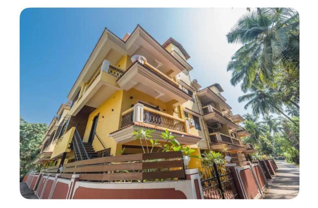 a yellow building with a palm tree in front of it at Avis Home in Calangute