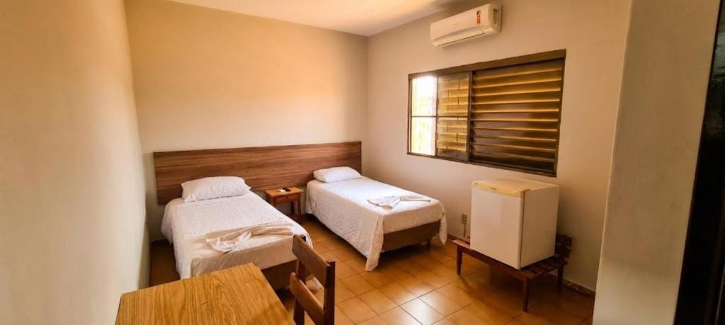 ein Zimmer mit zwei Betten, einem Tisch und einem Fenster in der Unterkunft Hotel Brivanna in Campo Grande