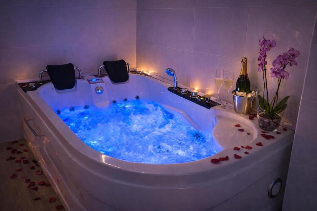 a bath tub filled with blue water with a bottle of wine at Apartamentos De la Haya & Suite con Jacuzzi, junto al Teatro Romano in Mérida