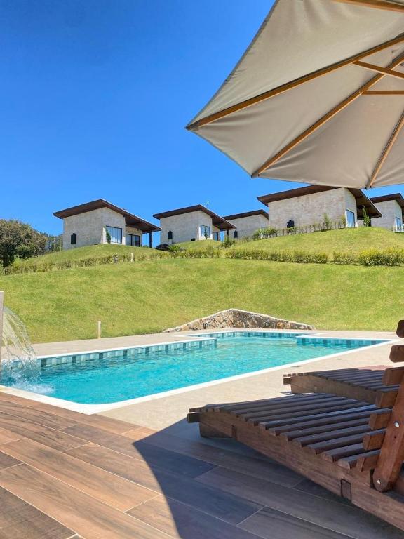 a swimming pool with an umbrella and a bench and an umbrella at Pousada Varandas de Minas in Monte Verde