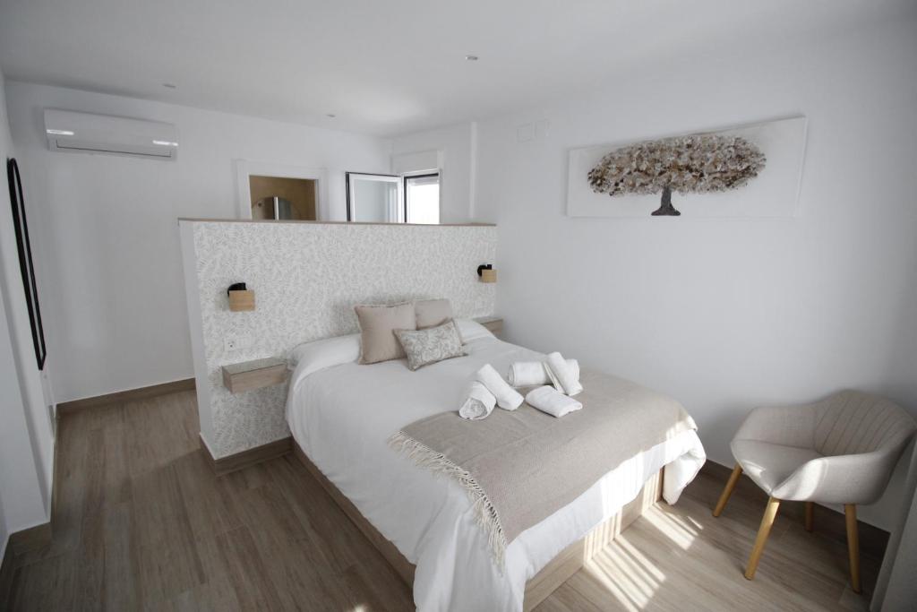 a white bedroom with a bed and a chair at LaJoya De La Villa in Priego de Córdoba