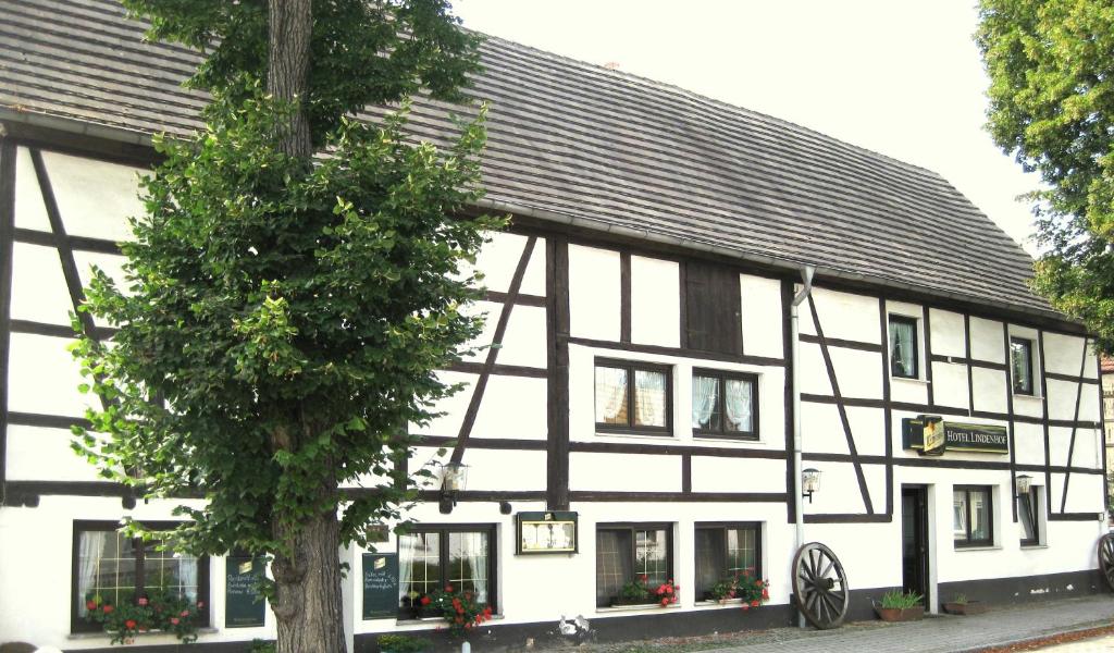 a black and white building with a tree in front of it at Hotel Lindenhof in Bad Lauchstädt