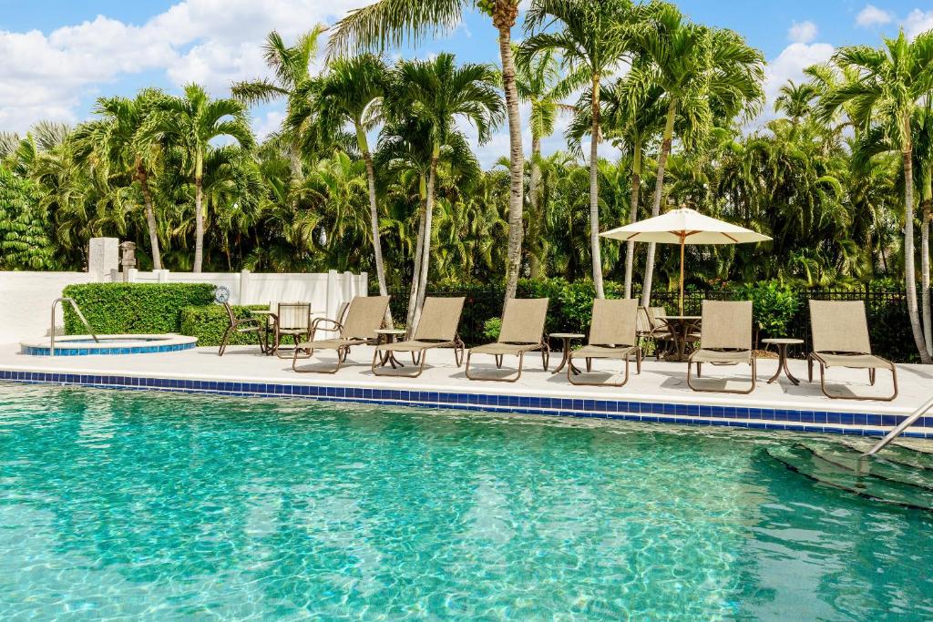 a pool with chairs and an umbrella and palm trees at Olde Marco Island Inn and Suites in Marco Island