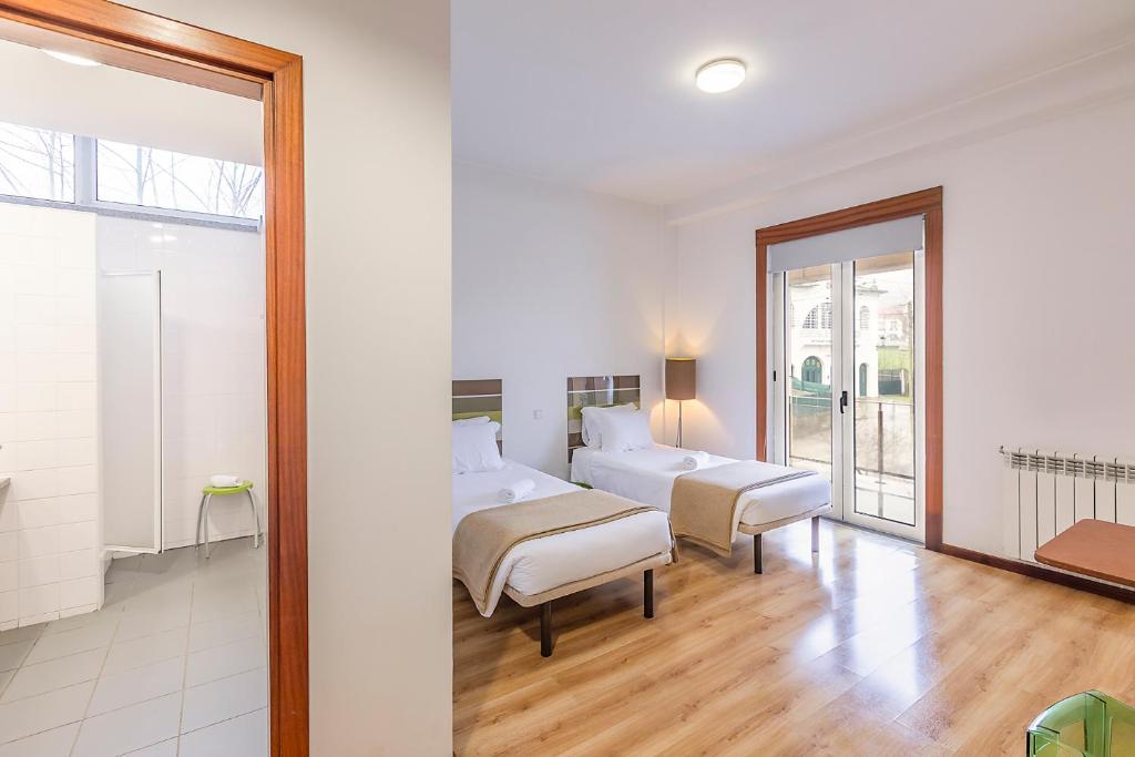 a white bedroom with two beds and a window at HI Lousã – Pousada de Juventude in Lousã