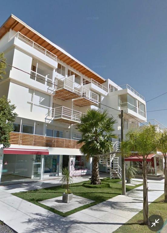 a large white building with palm trees in front of it at Departamento morderno y centrico-Paseo Plaza in Navarro