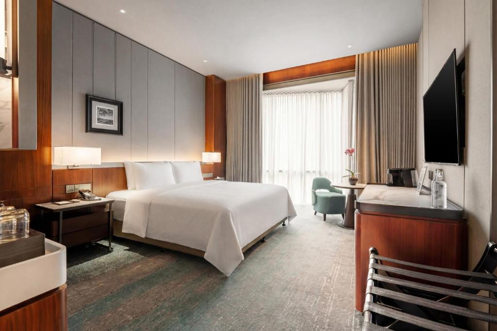 Spacious guest room with a large bed, desk, lounge chair and television cabinet.