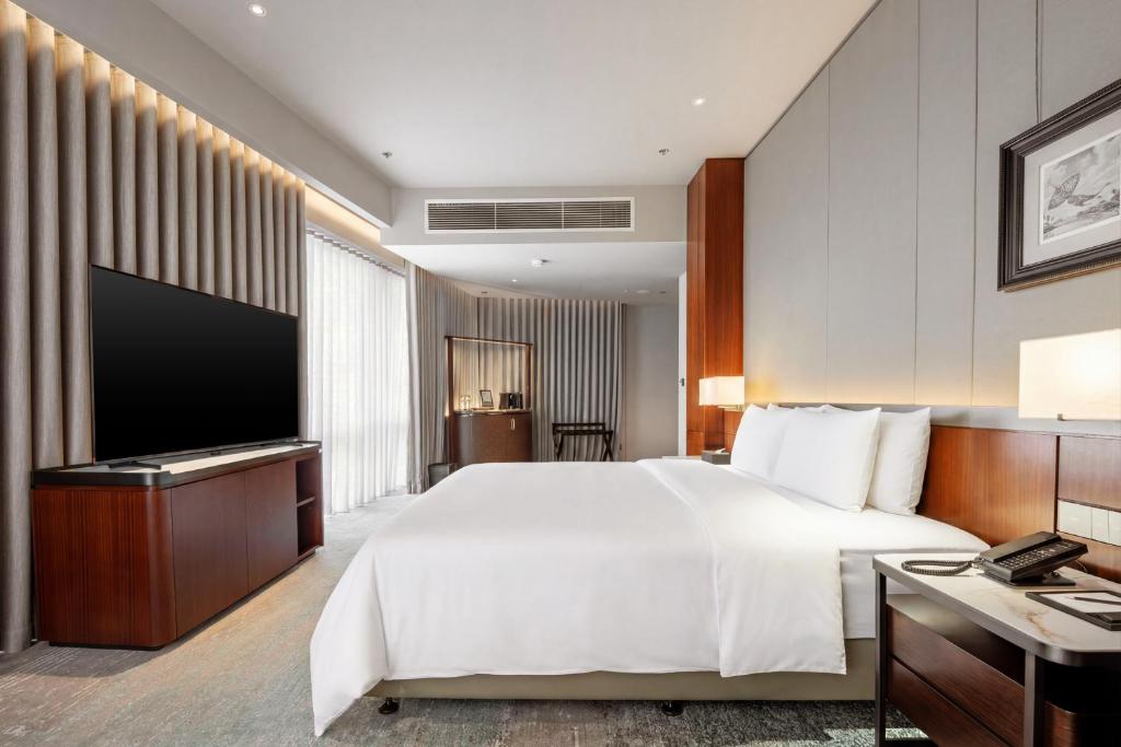 A polished king-style bedroom with a large television and a small seating area near the window.