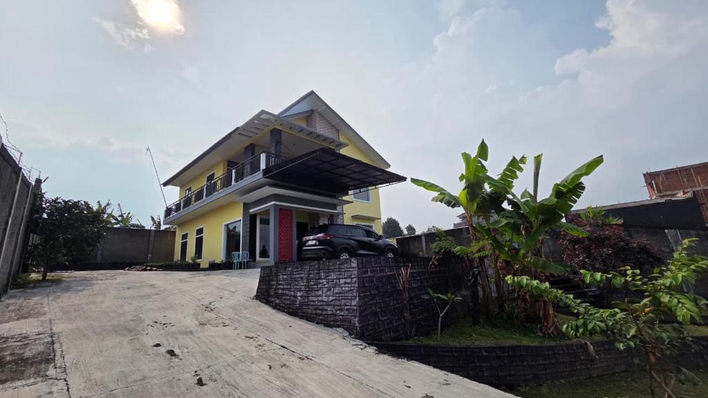 a yellow house with a car parked in the driveway at Mroom Villa Cipanas in Pacet