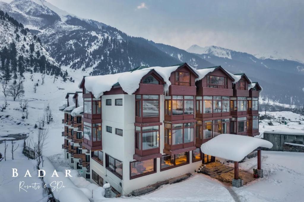 a building covered in snow with mountains in the background at Badar Resorts & Spa by Stay Pattern Riverside in Sonāmarg
