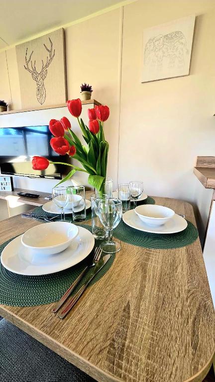 a table with plates and a vase of red tulips at Tea & Toast Cottage Seton Sands in Port Seton