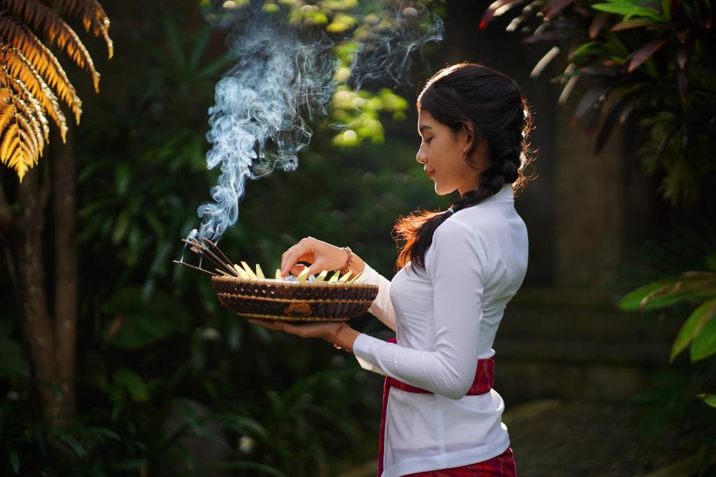 a woman holding a basket of food with smoke at Asri Sari Villa Ubud in Ubud