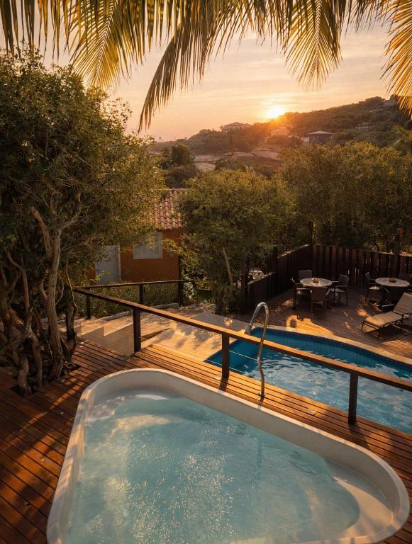 a hot tub on a deck with the sunset in the background at Calador Búzios Hotel in Búzios