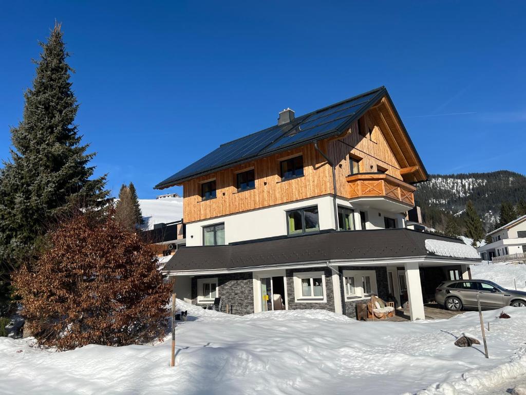a large house with a black roof in the snow at Ferienwohnung Bergblick in Filzmoos