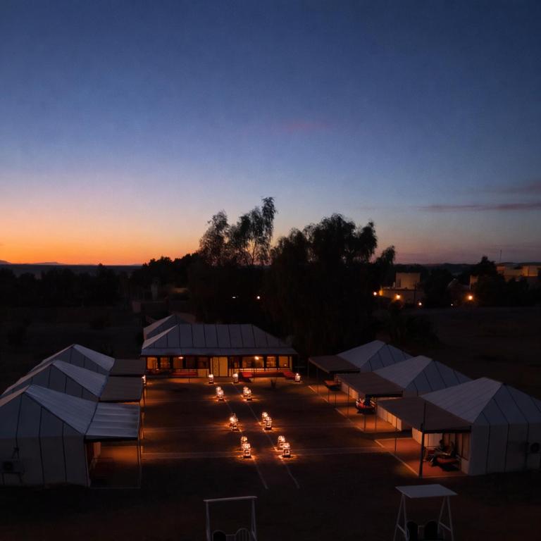 a group of tents in a parking lot at sunset at Milagro Luxury Camps in Merzouga