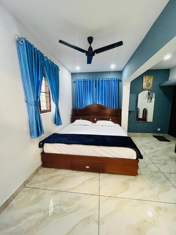 a bedroom with a bed with blue curtains and a ceiling fan at Nandbhavan Guruvayur in Guruvāyūr
