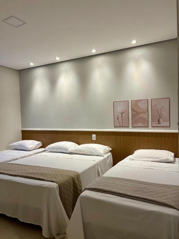 two beds in a room with three paintings on the wall at Pousada Bella in Vitória da Conquista