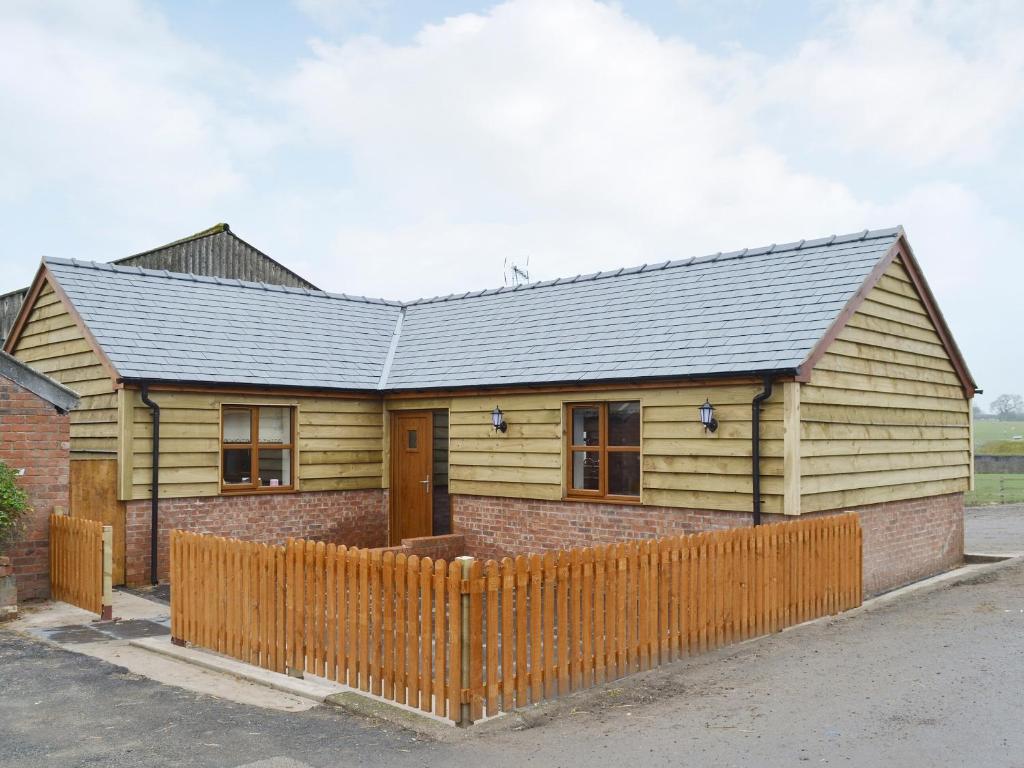 a wooden house with a fence in front of it at The Corn Store in Malpas