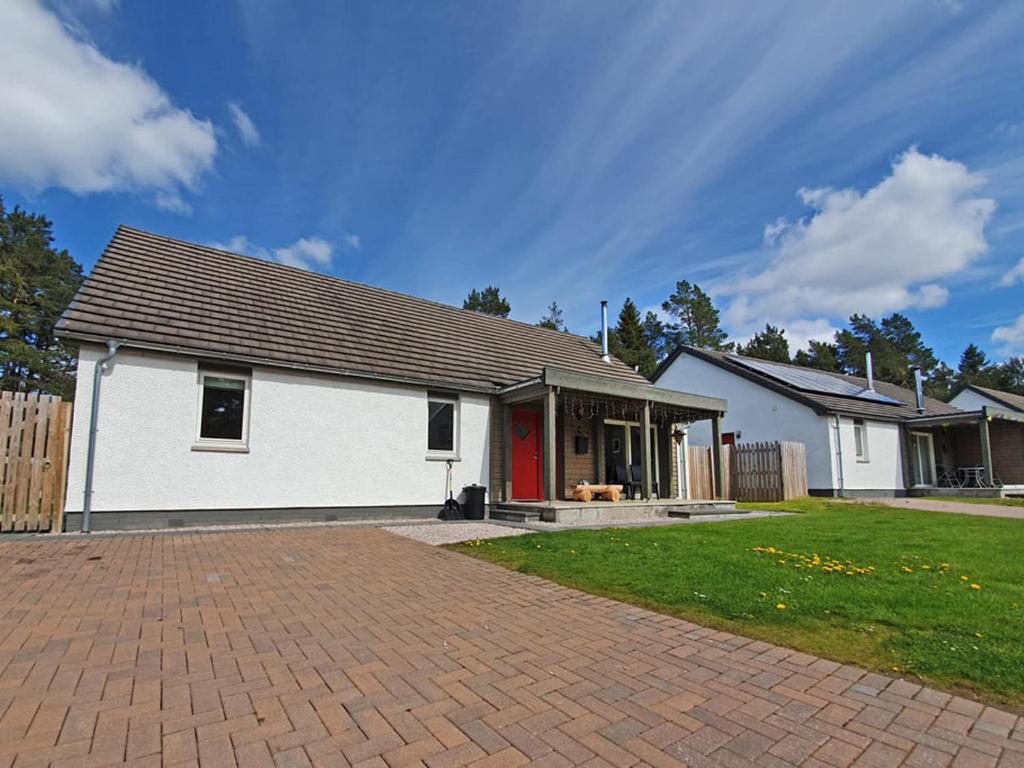 a white house with a red door in a yard at Delmhor No4 in Aviemore