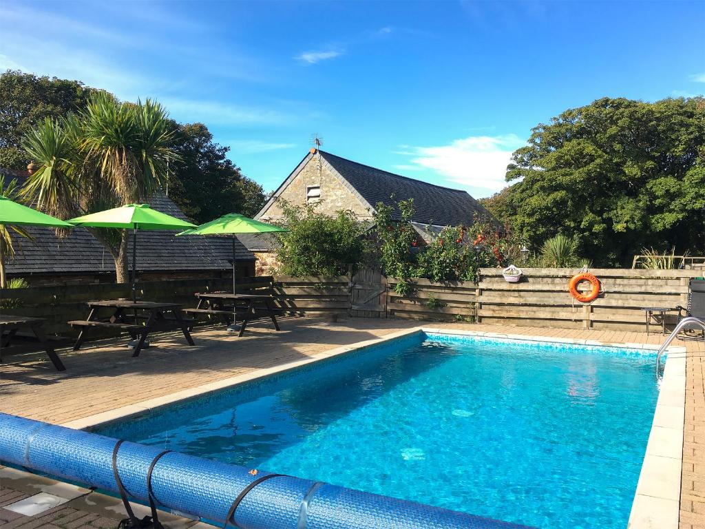 a swimming pool with tables and umbrellas next to a house at Porth Cottage- W40885 in Perranporth