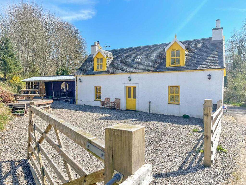 a white house with yellow windows and a wooden fence at Culrain Cottage in Fort Augustus
