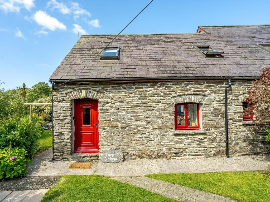 a stone house with a red door and windows at Honeysuckle - Uk35244 in Llanfyrnach