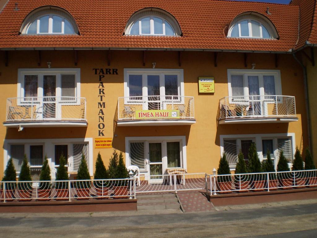 ein gelbes Gebäude mit Balkonen, Tischen und Bäumen in der Unterkunft Tarr-Tímea Apartmanok in Keszthely
