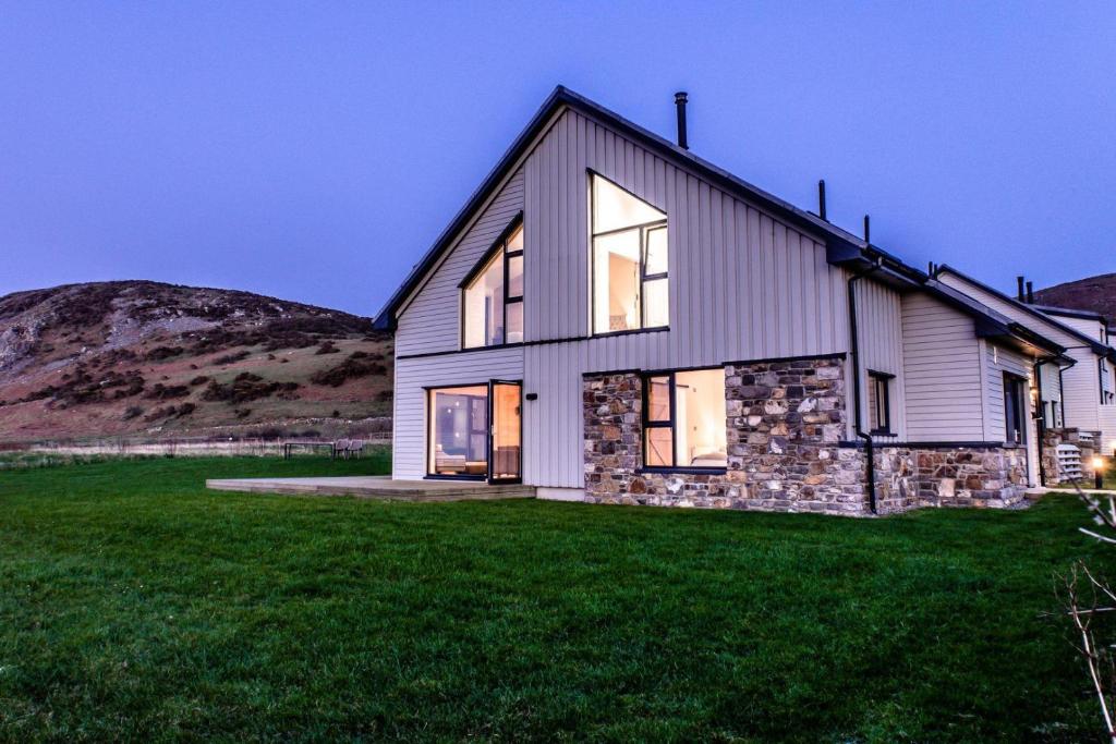 a house on a hill with a green lawn at Porthdinllaen by Together Travel - Luxury 5-Bed Holiday Retreat in Pistyll