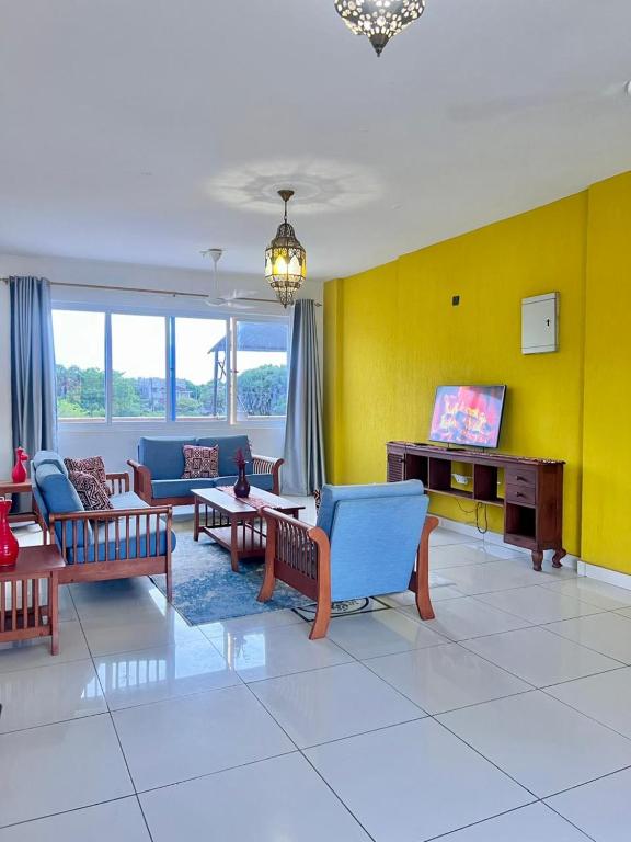 a living room with couches and a tv on a yellow wall at Diani Exquisite 3BR in Ukunda