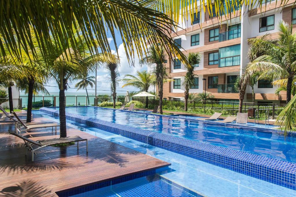 a swimming pool with palm trees and a building at Luxor Paulo Miranda Home Service in João Pessoa