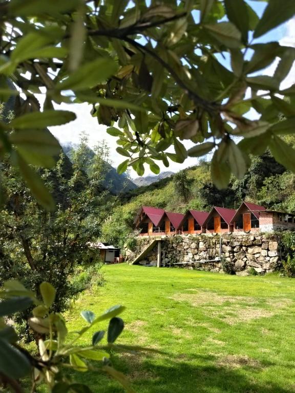 a stone building with red roofs in a green field at AndeStay Hostel Colpapampa in Colcapampa