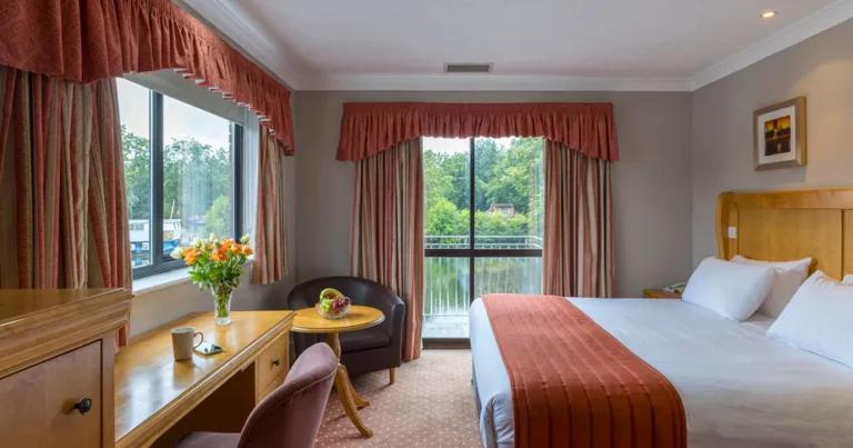 a hotel room with a bed and a desk and window at Lakeside International Hotel in Camberley