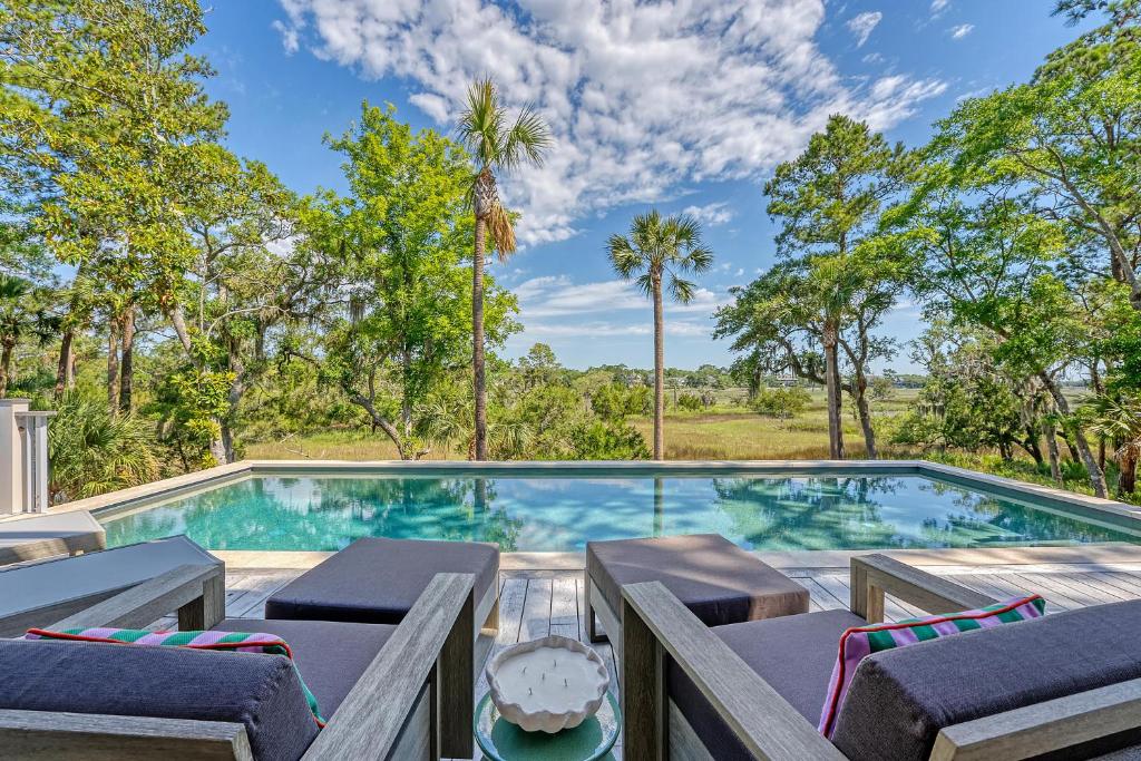 a swimming pool with chaise lounges and chairs in front of trees at 135 Halona Ln in Kiawah Island