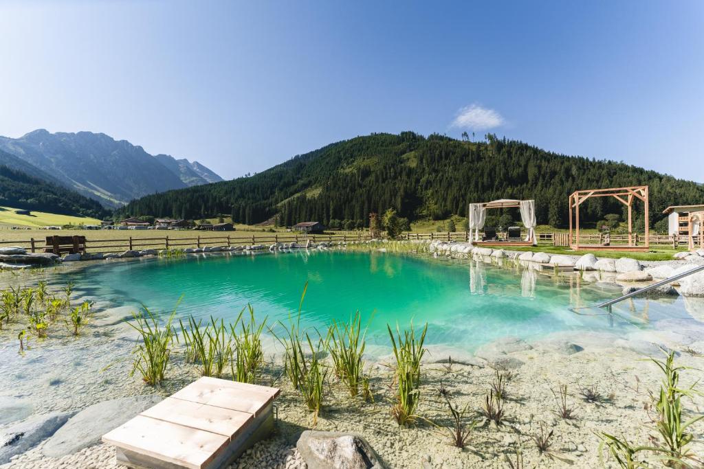 a pool of water with a bench in front of a mountain at Traumhotel Alpina - 4 Sterne Superior Luxushotel, hoteleigenen Badesee, Adults Only in Gerlos