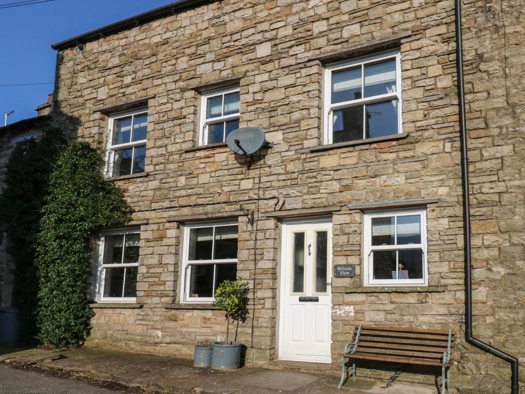 a brick building with a white door and a bench at Hillside View in Hawes