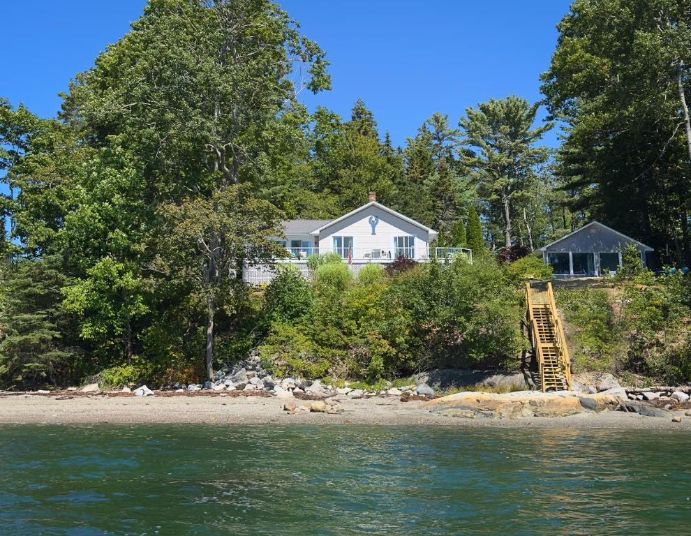 a house on the shore of a beach with a ladder at Lucky Stone Retreat - private beach & Acadia view in Sullivan
