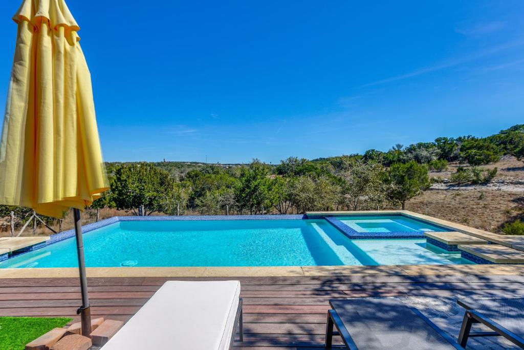 a swimming pool with an umbrella and a table and a swimming pool at Infinity Edge Pool & Fire Pit: Spicewood Getaway! in Spicewood