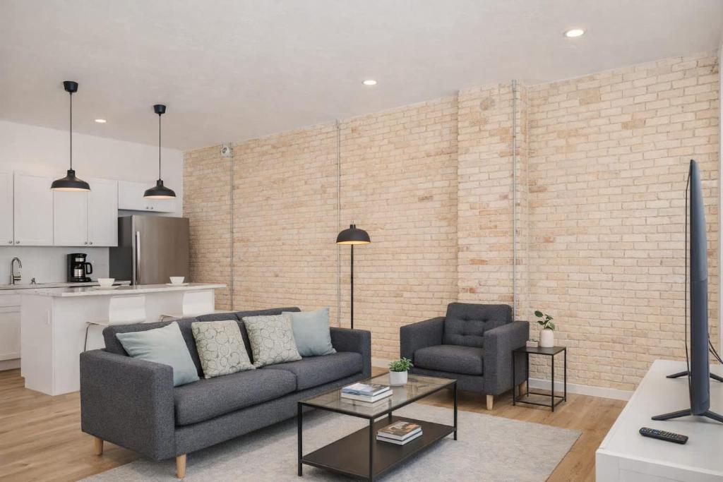 a living room with a couch and two chairs and a brick wall at Luxury Downtown 2 Bedroom Flat in Neenah