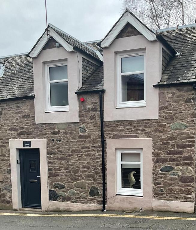 a brick house with a dog in the window at Meadow Cottage in Crieff