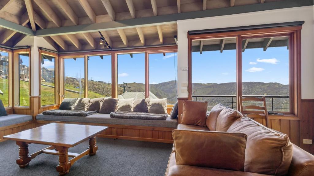 a living room with couches and a table and windows at Eagles Nest in Mount Hotham