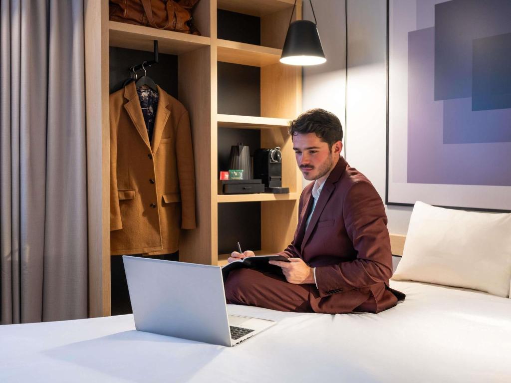a man in a suit sitting on a bed with a laptop at Ibis Orly Chevilly Tram 7 in Chevilly-Larue