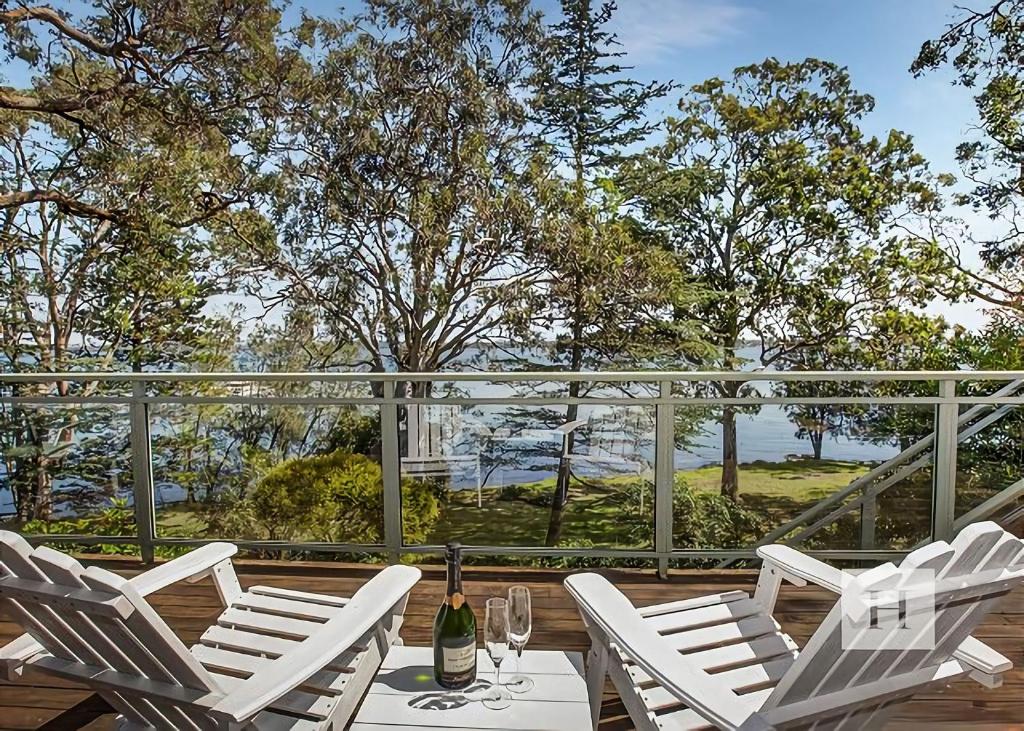 a patio with white chairs and a table with a bottle of wine at Niaroo Lakeside in Summerland Point
