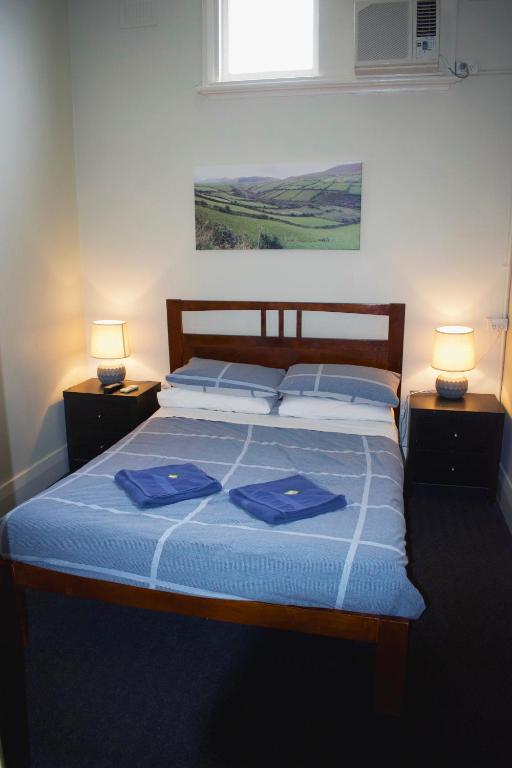 a bedroom with a bed with blue sheets and two lamps at Jack Duggans Pub in Bathurst